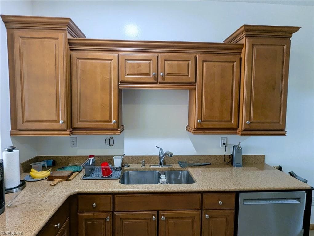 Kitchen with dishwasher, light stone countertops, and brown cabinetry