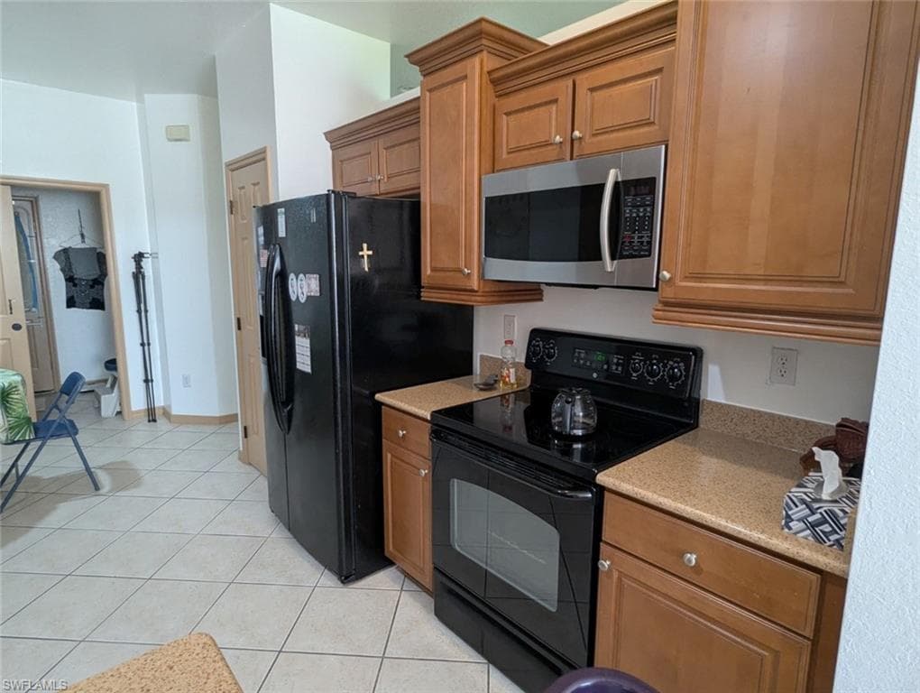 Kitchen with electric range, stainless steel microwave, brown cabinets, light tile patterned flooring, and light stone counters