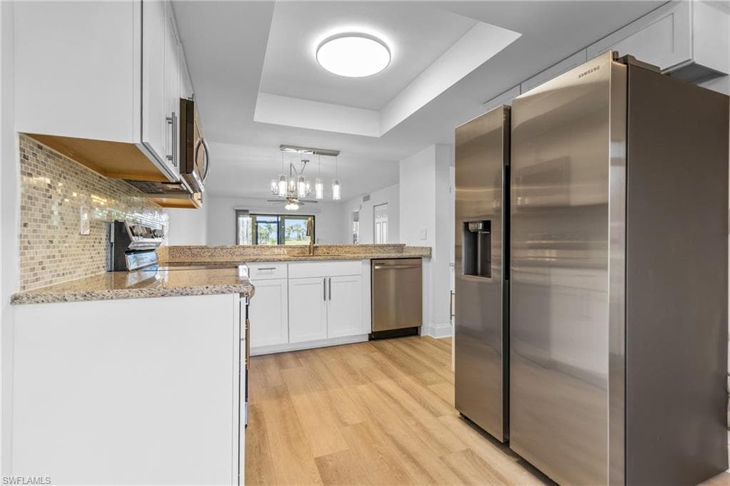 Kitchen featuring stainless steel appliances, a raised ceiling, white cabinetry, and light stone counters
