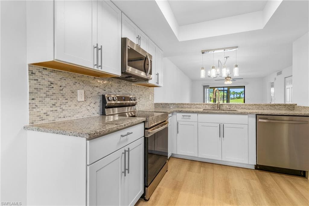 Kitchen featuring stainless steel appliances, light wood finished floors, light stone countertops, a raised ceiling, and white cabinets