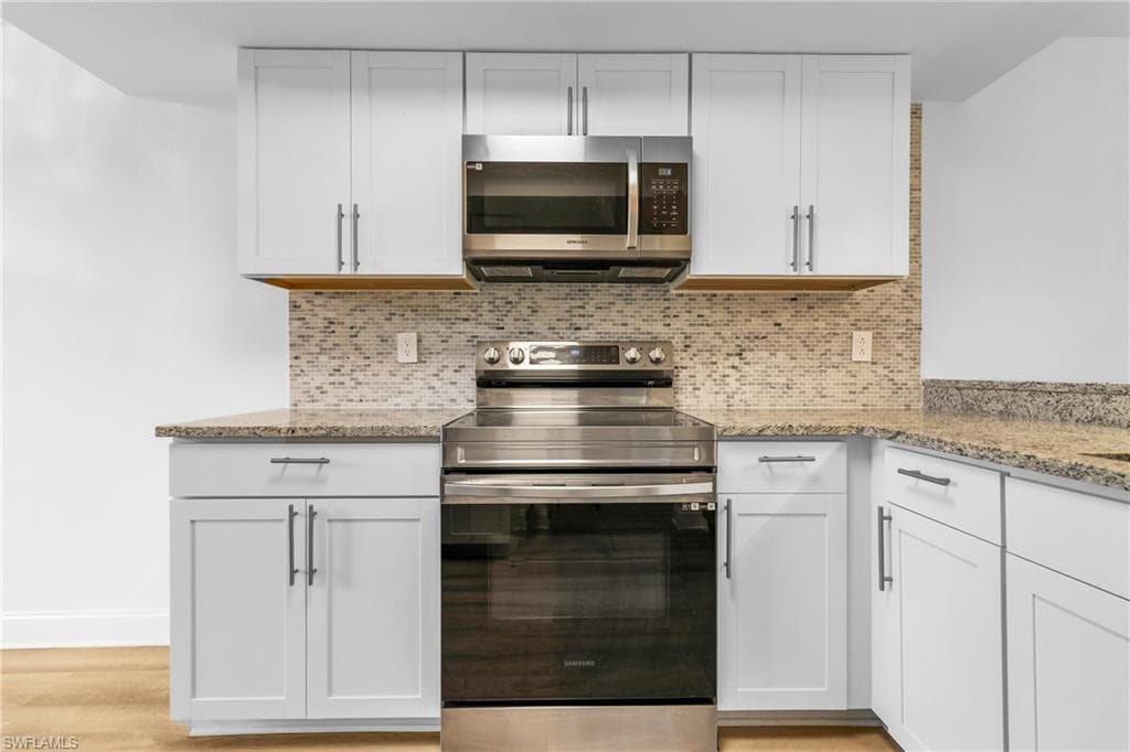 Kitchen with appliances with stainless steel finishes, light stone countertops, white cabinets, and decorative backsplash
