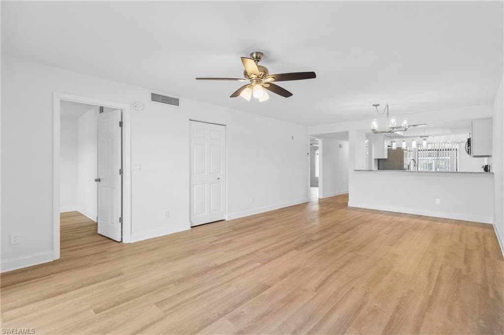 Unfurnished living room with light wood-style flooring, a chandelier, and a ceiling fan