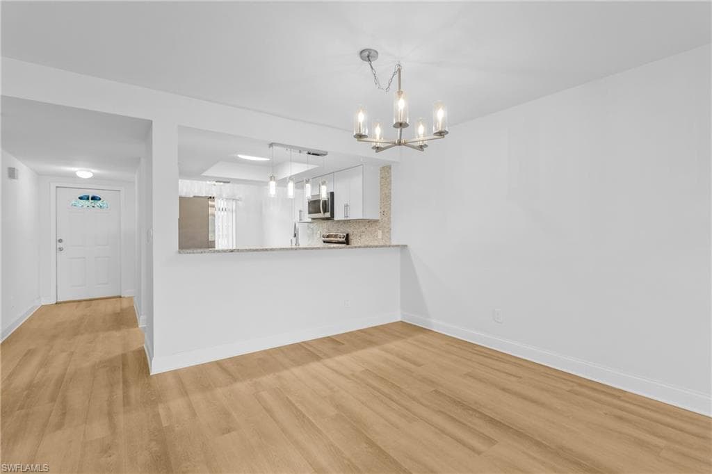 Unfurnished living room featuring light wood finished floors and a chandelier