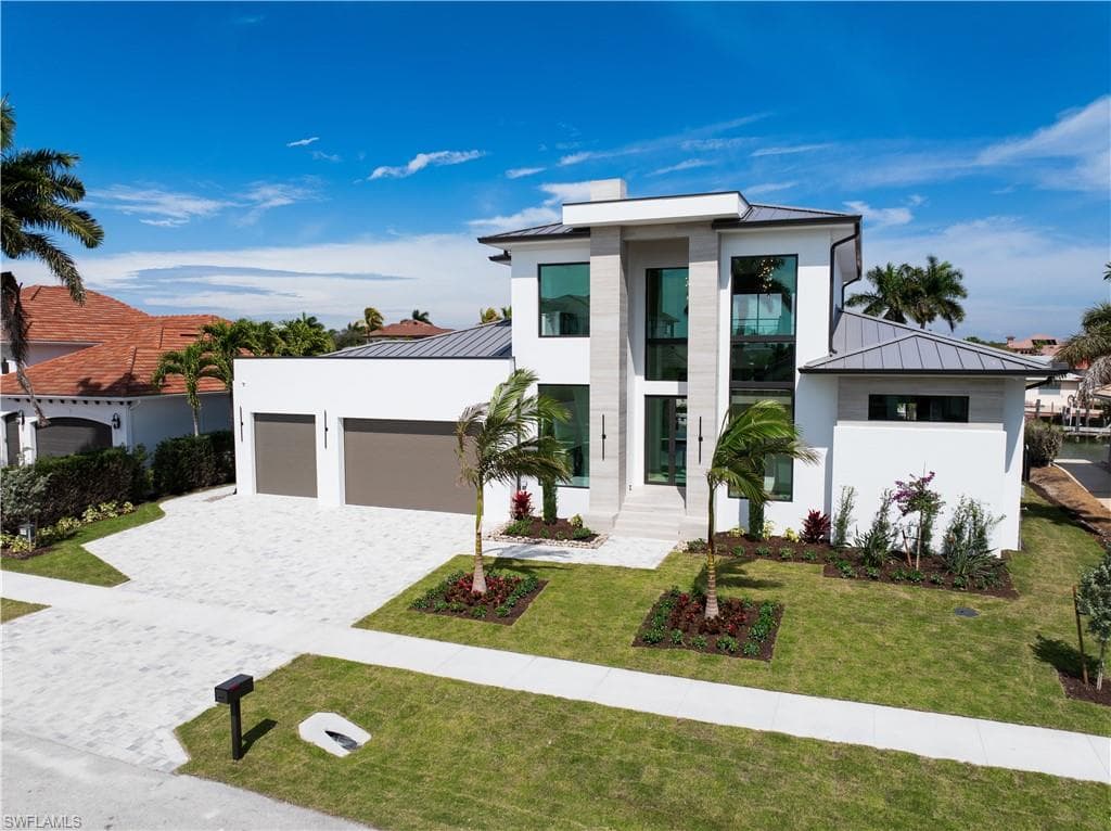 Contemporary home featuring a standing seam roof, a garage, decorative driveway, a front yard, and stucco siding