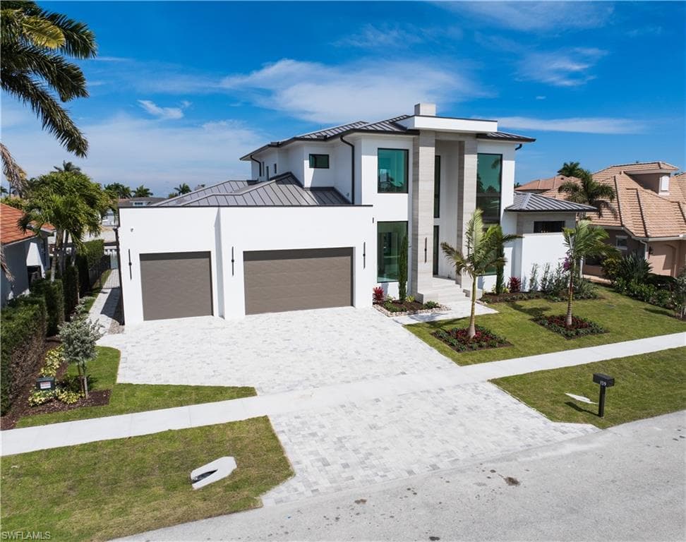 Contemporary home featuring a standing seam roof, a garage, a front yard, decorative driveway, and stucco siding