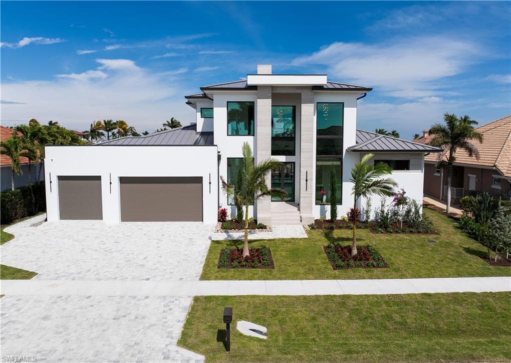 Modern home with a standing seam roof, a garage, decorative driveway, and a front yard