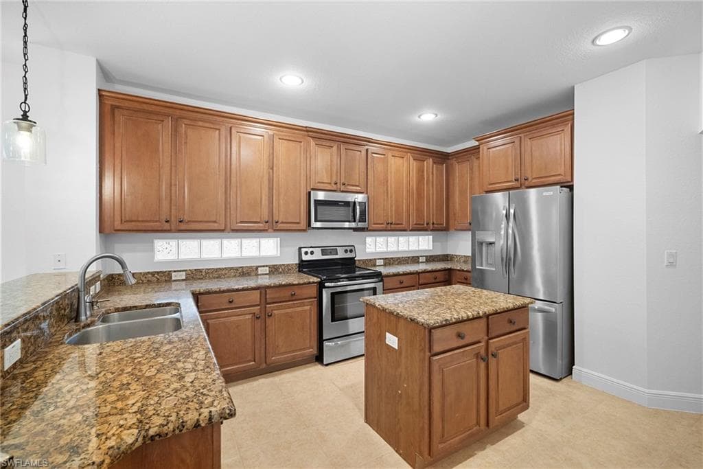 Kitchen with brown cabinetry, stainless steel appliances, dark stone countertops, pendant lighting, and recessed lighting