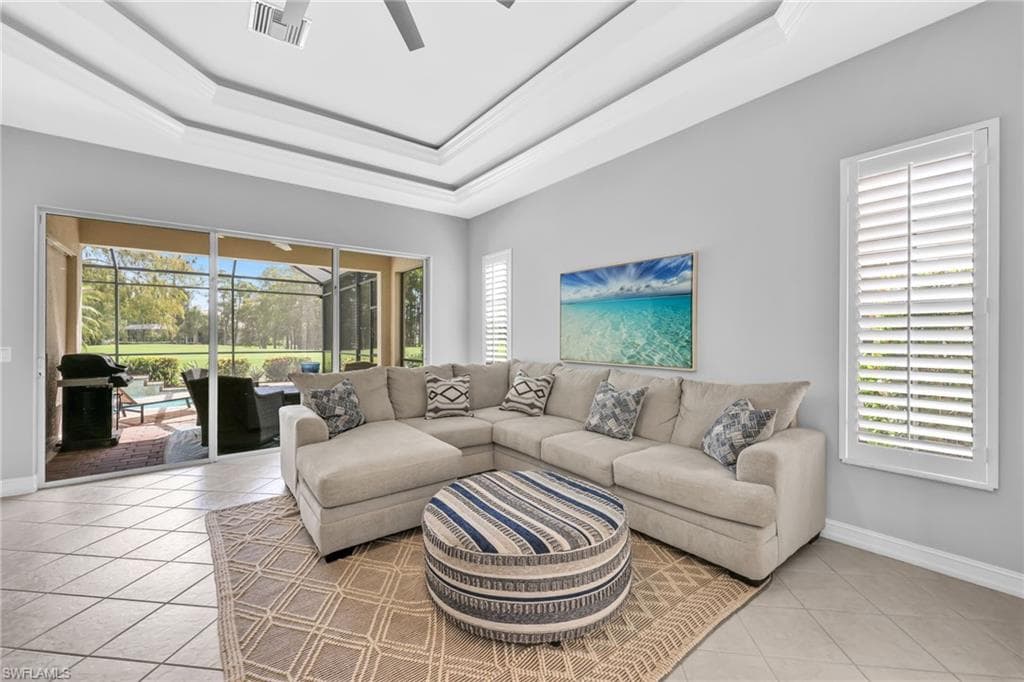 Bright, spacious, open and airy Family room featuring light tile patterned floors, ceiling fan, and a tray ceiling with views of golf course.