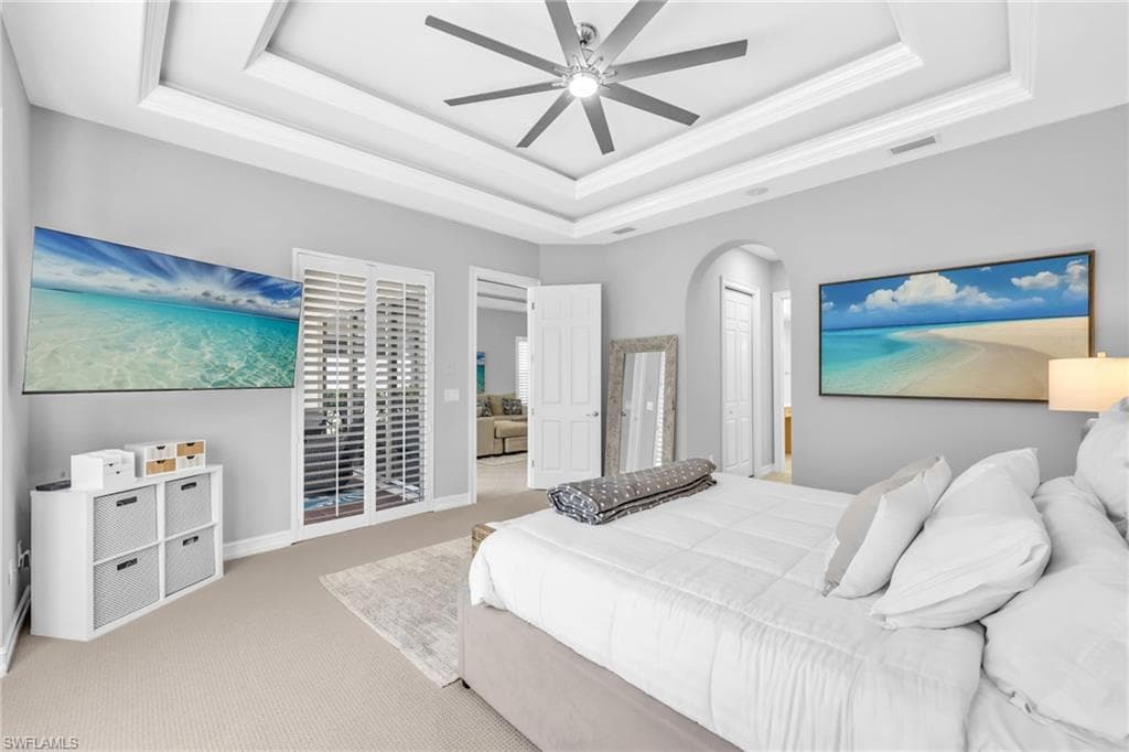 Bedroom with carpet flooring, a raised ceiling, ceiling fan, arched walkways, and a closet