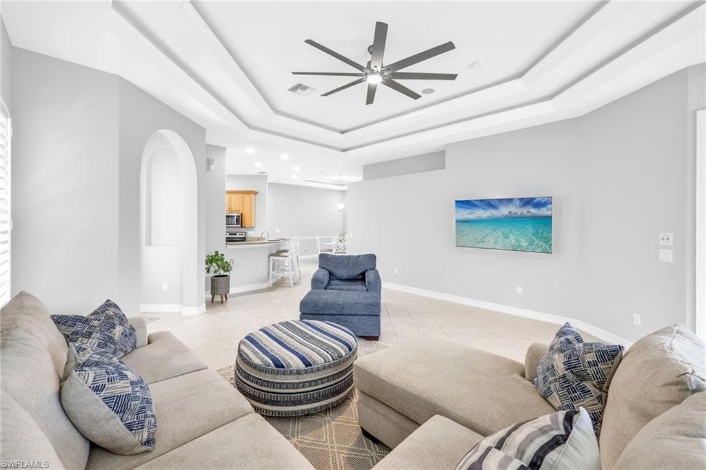 Bright, spacious, open and airy Family room featuring light tile patterned floors, ceiling fan, and a tray ceiling.
