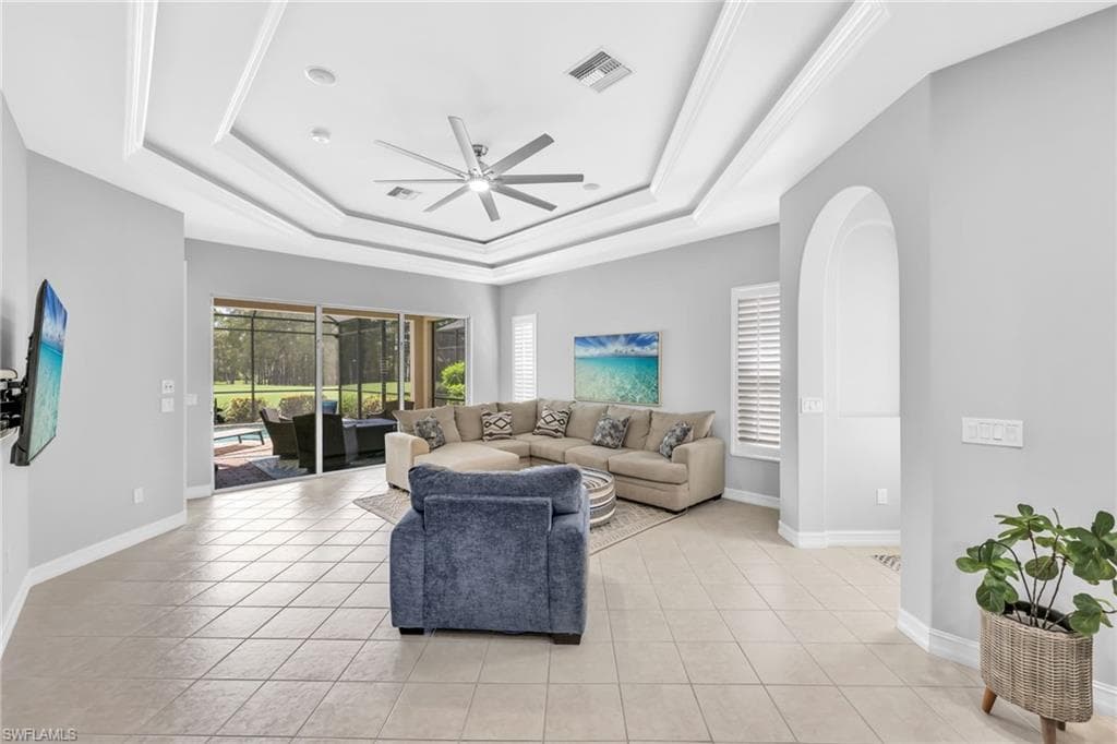 Living room with ceiling fan, a sunroom, light tile patterned floors, and a tray ceiling