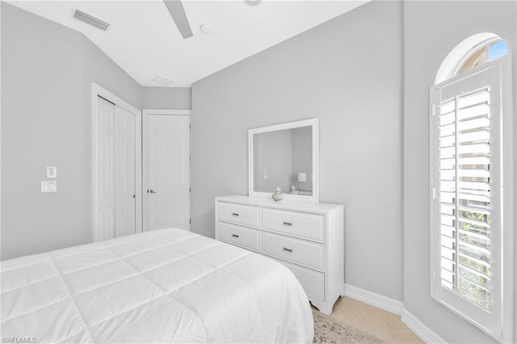 Bedroom featuring multiple windows, light tile patterned floors, ceiling fan, and a closet