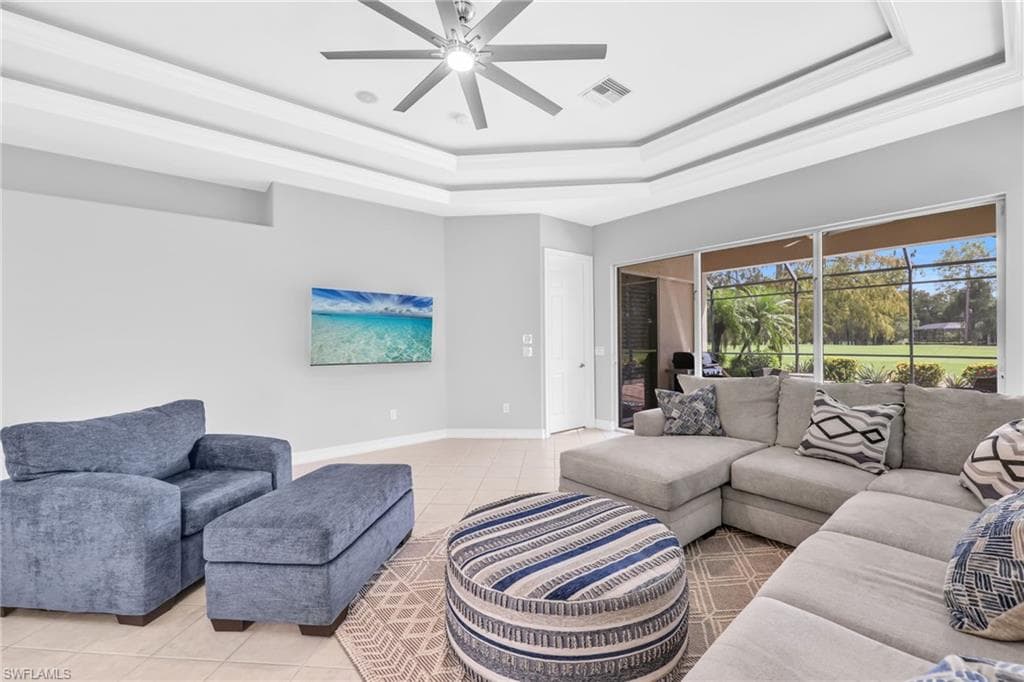 Family room area with a tray ceiling, light tile patterned flooring, a ceiling fan, and view of golf course and outdoor patio