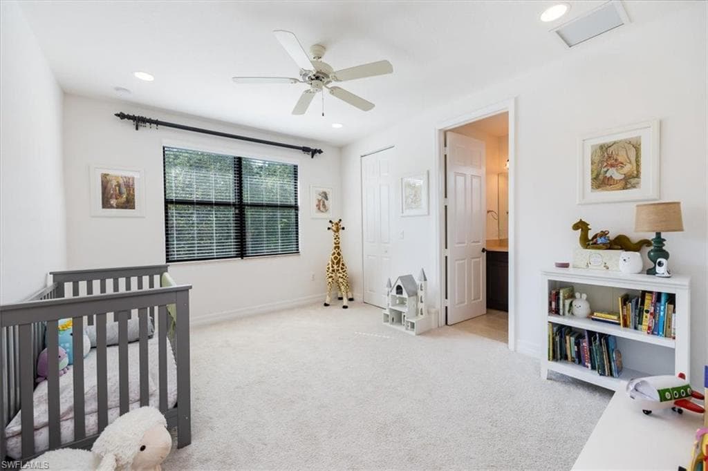 Bedroom featuring light carpet, ceiling fan, connected bathroom, a closet, and a crib