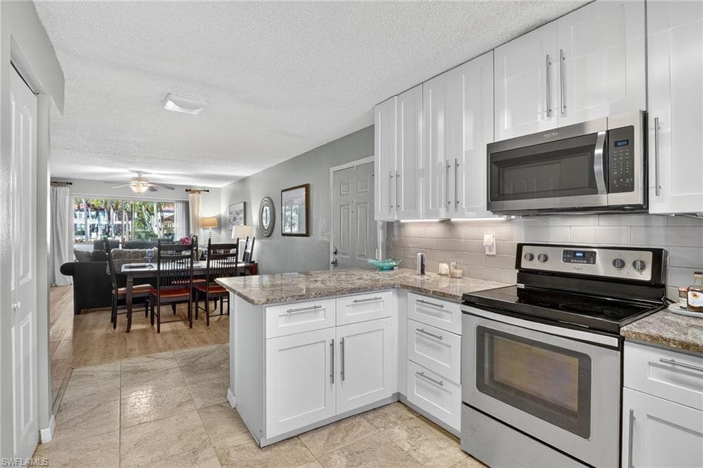Kitchen with appliances with stainless steel finishes, white cabinets, a peninsula, backsplash, and light stone countertops