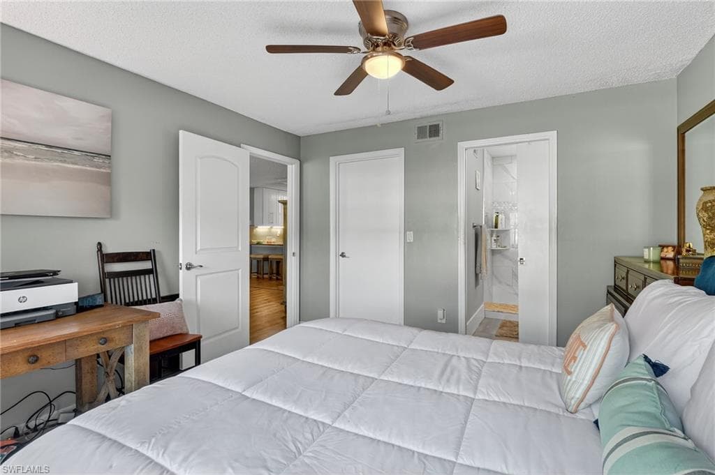Bedroom with a textured ceiling, a ceiling fan, connected bathroom, and wood finished floors