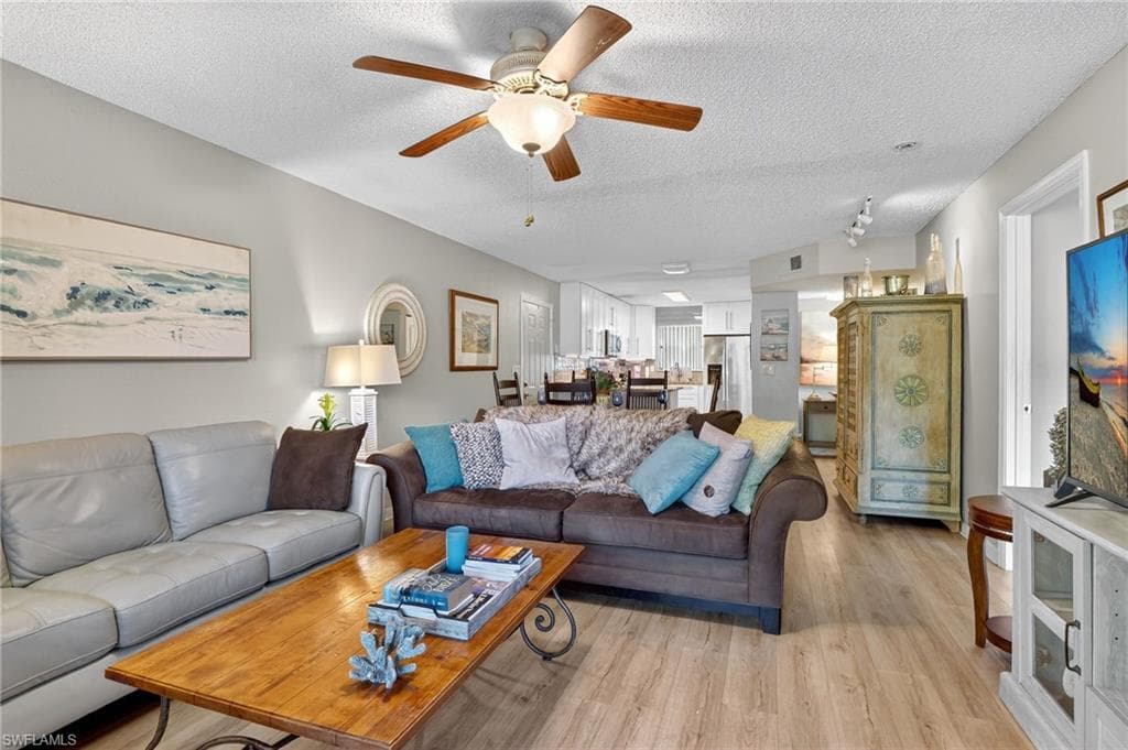 Living room with a textured ceiling, light wood-style floors, and ceiling fan