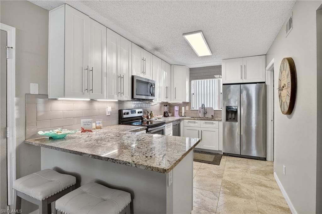 Kitchen featuring appliances with stainless steel finishes, light stone counters, white cabinets, a breakfast bar area, and a peninsula