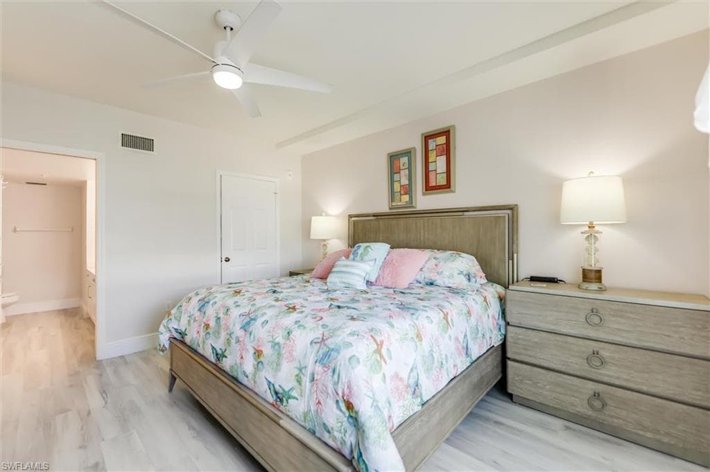Bedroom with light wood-style floors, ceiling fan, and connected bathroom