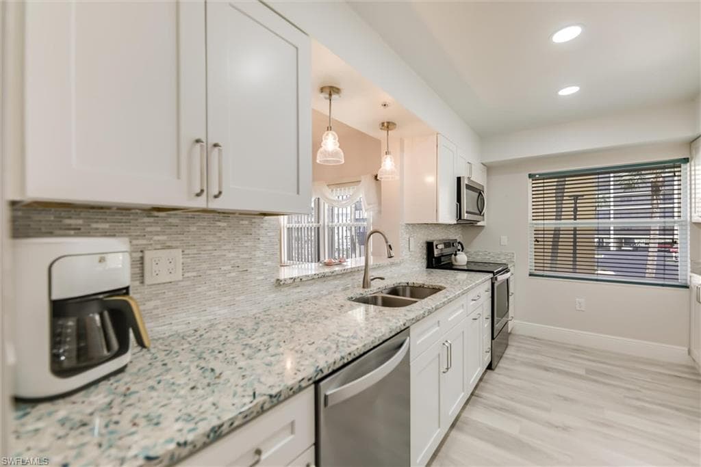 Kitchen featuring appliances with stainless steel finishes, decorative backsplash, white cabinetry, recessed lighting, and light stone counters