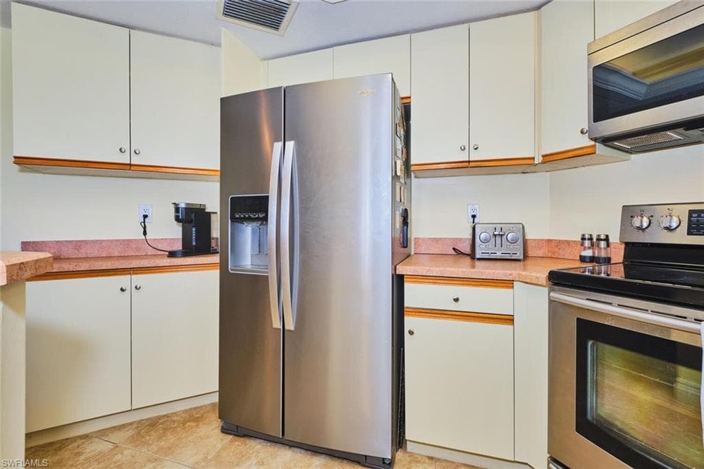 Kitchen featuring appliances with stainless steel finishes, light countertops, light tile patterned floors, and white cabinetry