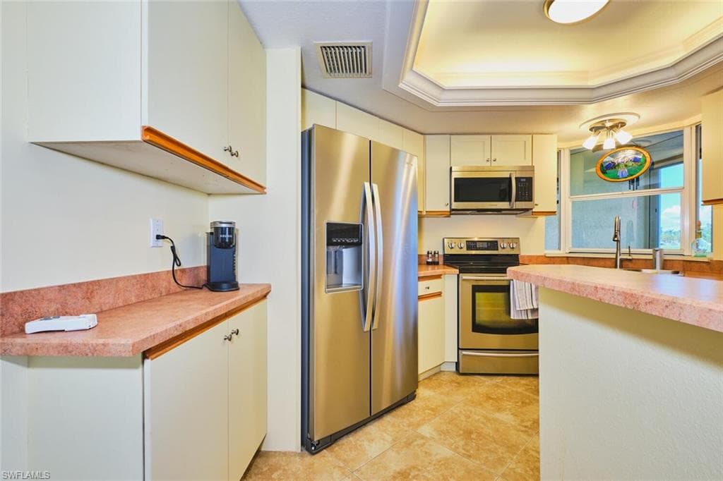 Kitchen featuring appliances with stainless steel finishes, a raised ceiling, light countertops, crown molding, and light tile patterned floors