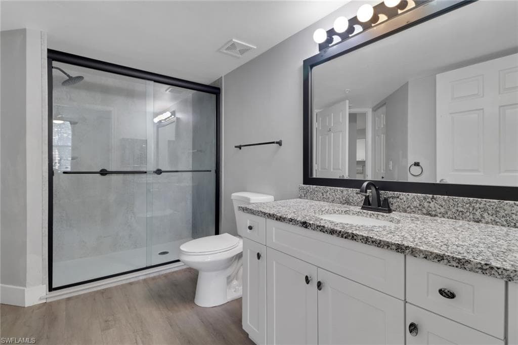 Full bath with a shower stall, vanity, and light wood finished floors