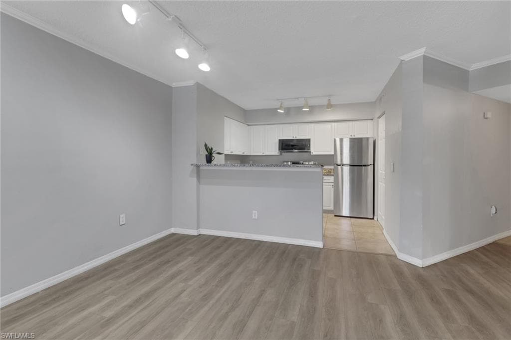Kitchen with a peninsula, white cabinets, freestanding refrigerator, light wood-style flooring, and crown molding
