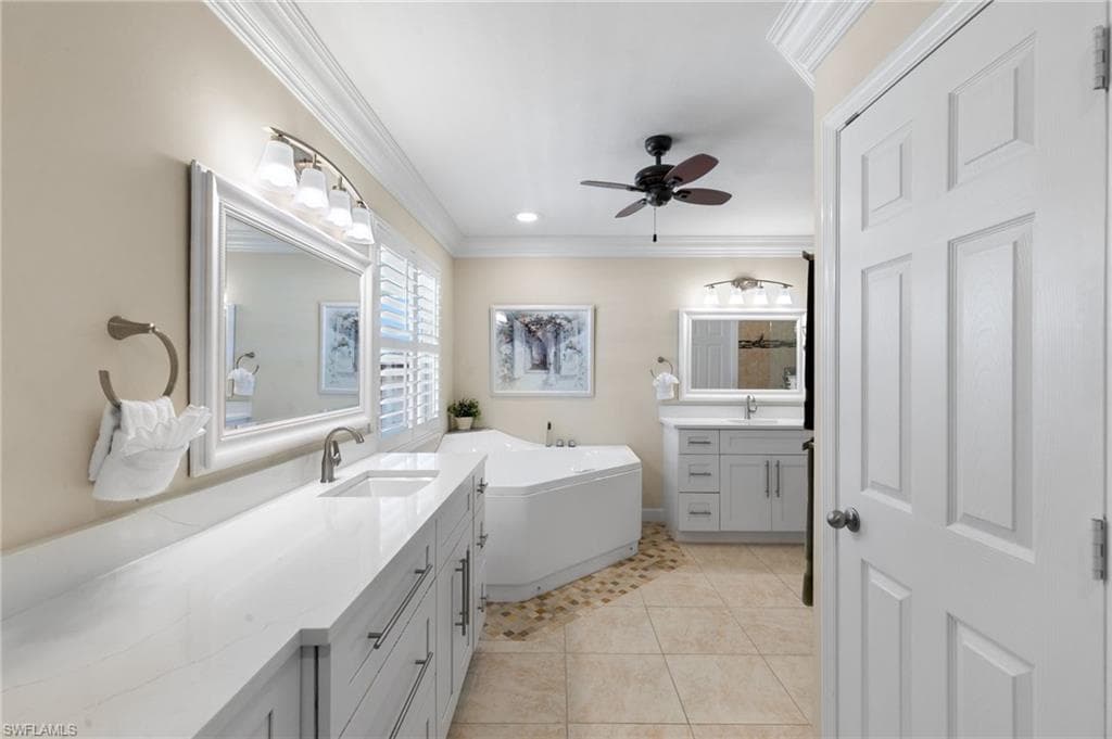 Bathroom with two vanities, light tile patterned flooring, crown molding, a freestanding tub, and ceiling fan