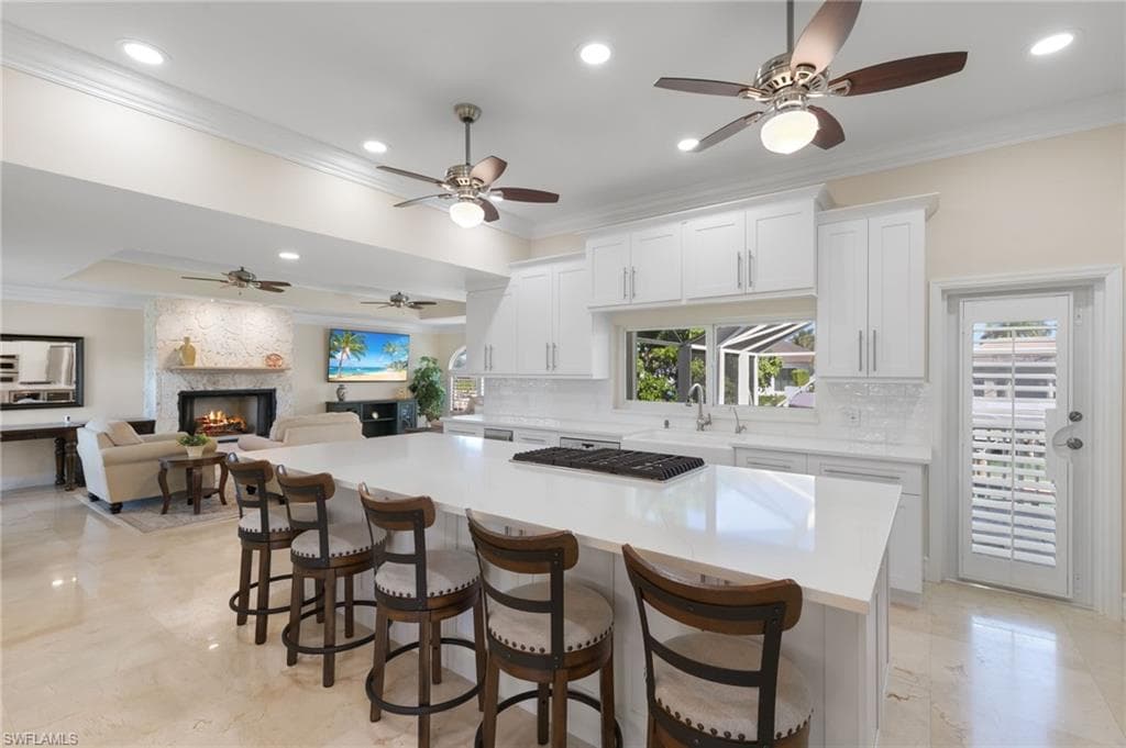 Kitchen with crown molding, a large fireplace, white cabinets, a center island, and decorative backsplash