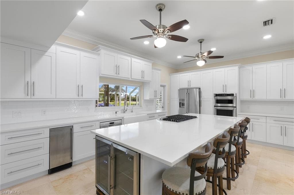 Kitchen featuring ornamental molding, white cabinetry, a kitchen bar, appliances with stainless steel finishes, and recessed lighting