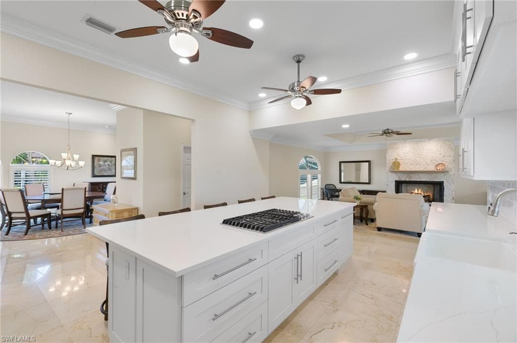 Kitchen featuring a kitchen breakfast bar, ornamental molding, a fireplace, white cabinets, and open floor plan