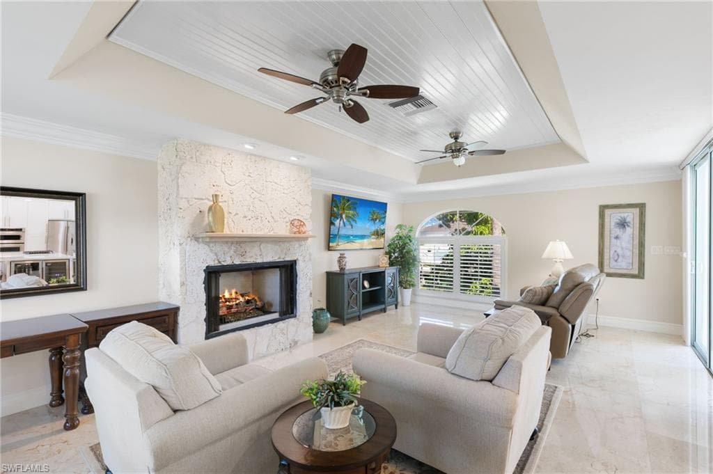 Living area featuring a tray ceiling, ornamental molding, a stone fireplace, and a ceiling fan