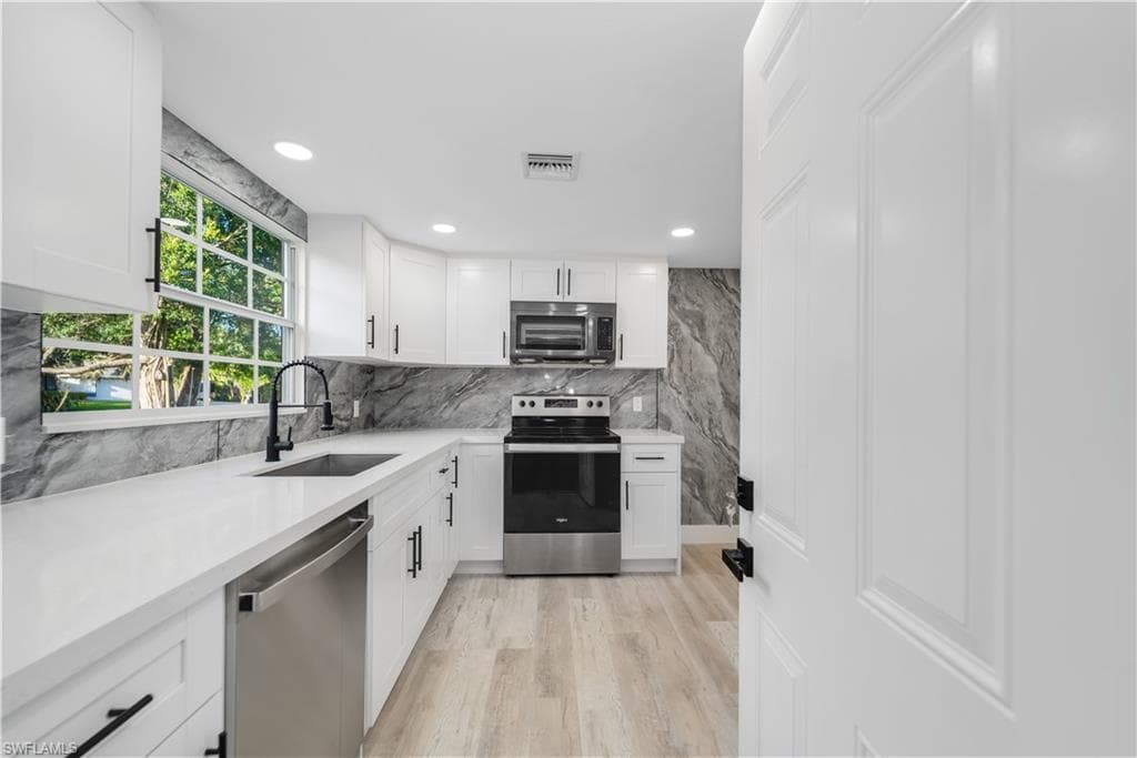 Kitchen with stainless steel appliances, white cabinets, light stone counters, recessed lighting, and tasteful backsplash