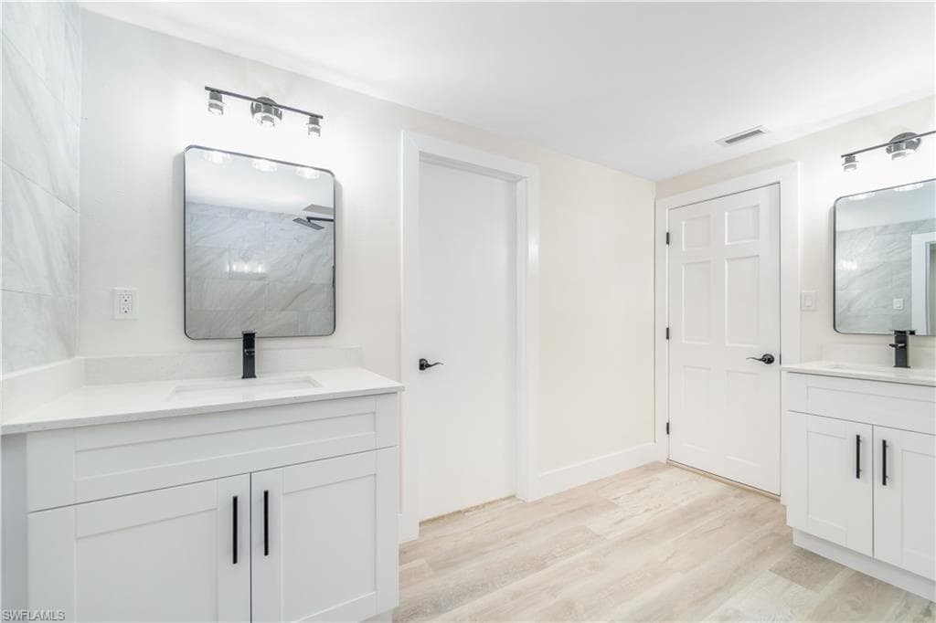 Full bath featuring a tile shower, two vanities, and light wood-style floors