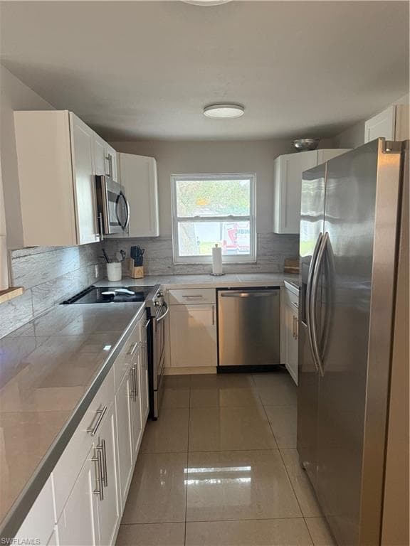 Kitchen featuring tasteful backsplash, dishwasher, refrigerator, stove, and white cabinetry