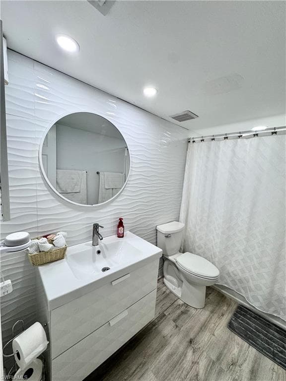 Bathroom with curtained shower, vanity, tile walls, wood finished floors, and recessed lighting