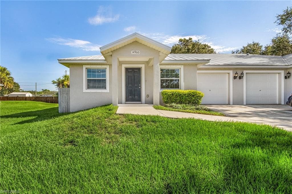 View of front of property with stucco siding, a metal roof, a garage, and driveway