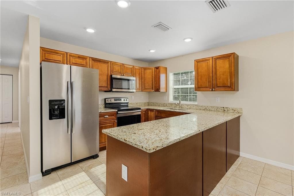 Kitchen featuring stainless steel appliances, light stone counters, a peninsula, brown cabinets, and recessed lighting
