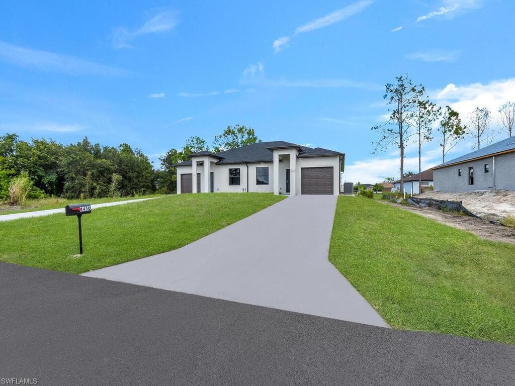 View of front facade with an attached garage, driveway, a front yard, and stucco siding