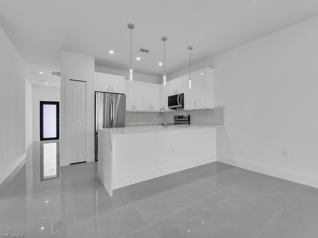 Kitchen with white cabinets, modern cabinets, hanging light fixtures, a peninsula, and stainless steel appliances