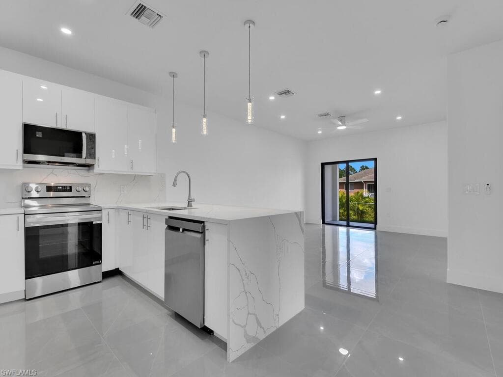 Kitchen with a peninsula, hanging light fixtures, white cabinets, appliances with stainless steel finishes, and light stone countertops