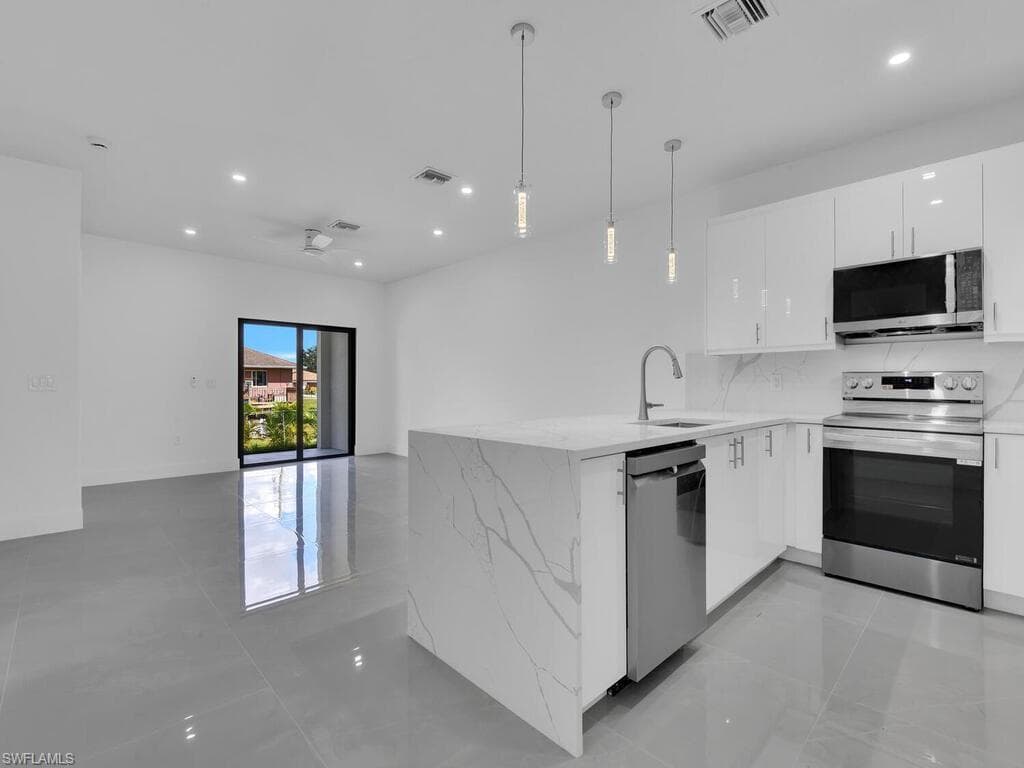 Kitchen featuring a peninsula, appliances with stainless steel finishes, white cabinets, light stone counters, and recessed lighting