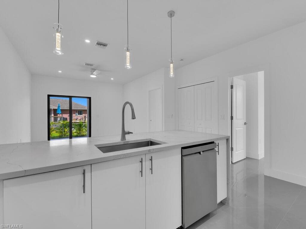 Kitchen with decorative light fixtures, light stone countertops, stainless steel dishwasher, white cabinets, and recessed lighting