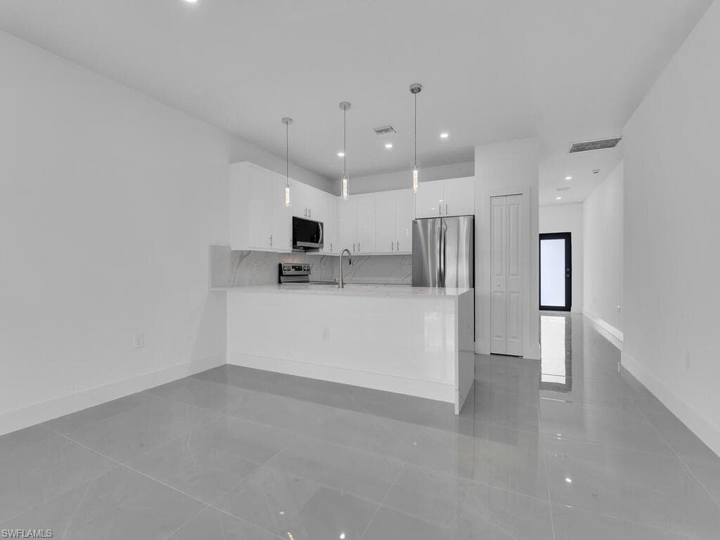 Kitchen featuring white cabinetry, appliances with stainless steel finishes, decorative light fixtures, light tile patterned floors, and a peninsula