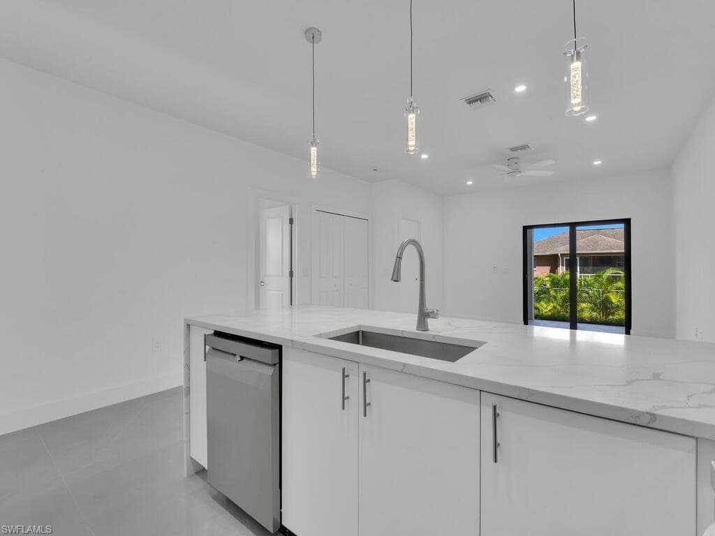 Kitchen with light stone counters, hanging light fixtures, recessed lighting, stainless steel dishwasher, and a ceiling fan