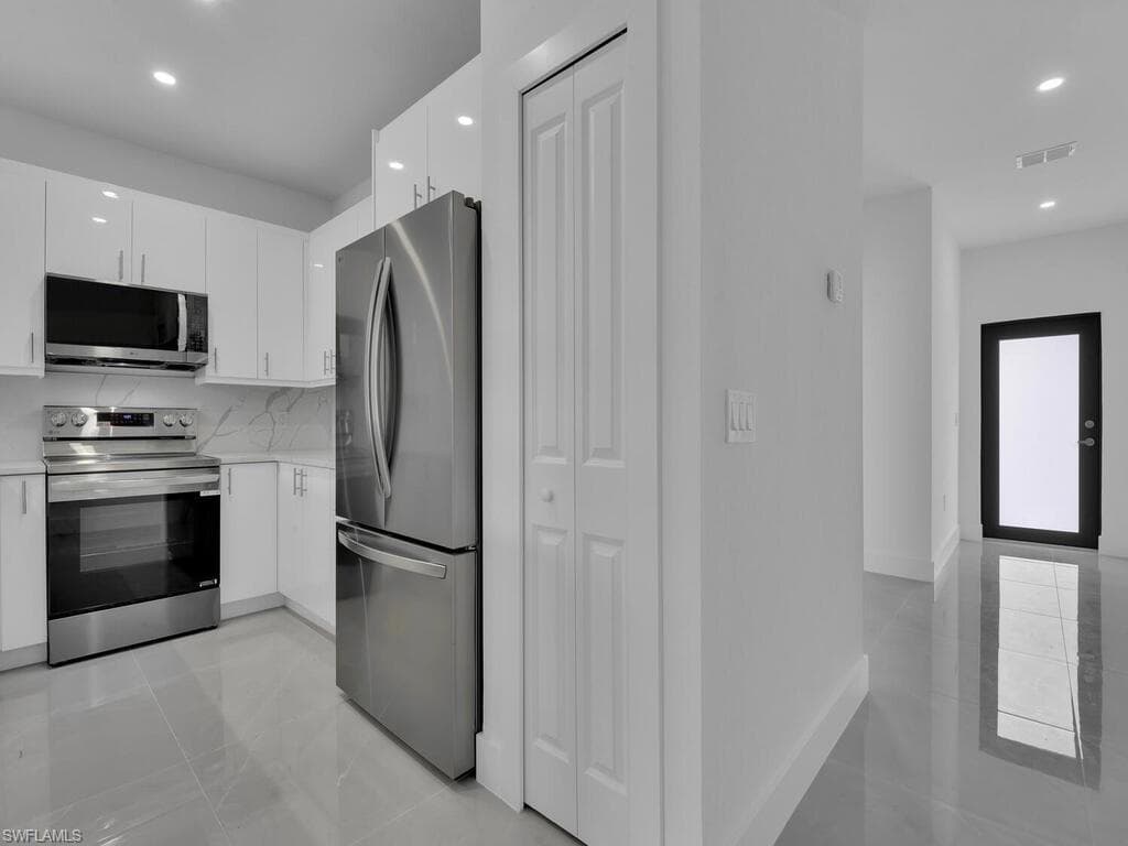 Kitchen with stainless steel appliances, recessed lighting, white cabinets, light stone counters, and modern cabinets