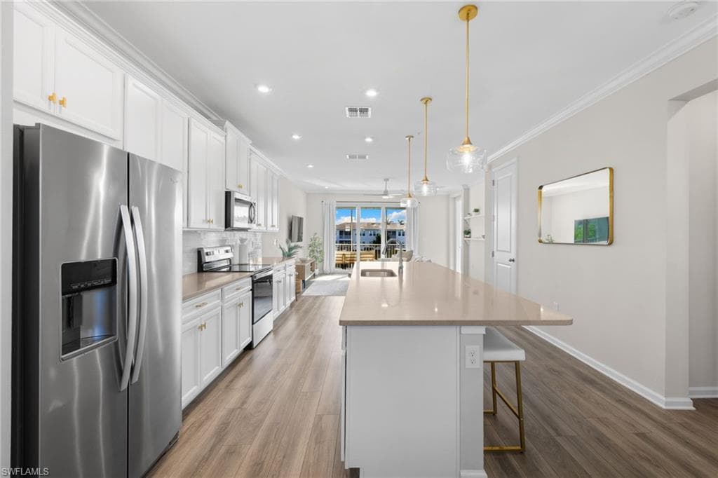 Kitchen featuring appliances with stainless steel finishes, white cabinetry, a breakfast bar, a center island with sink, and light wood-style flooring