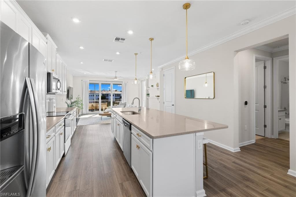 Kitchen featuring appliances with stainless steel finishes, white cabinets, an island with sink, dark wood-style floors, and recessed lighting
