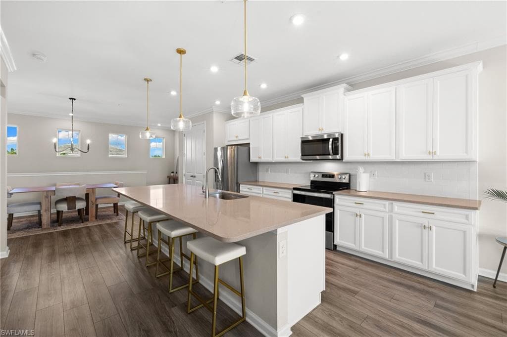 Kitchen with a breakfast bar area, stainless steel appliances, an island with sink, hanging light fixtures, and decorative backsplash